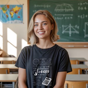 May include: A black t-shirt with white mathematical equations and a calculator graphic. The shirt features the square root of 4489 and other formulas. A smiling person is wearing the shirt in a classroom setting.