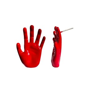 May include: A pair of red hand-shaped earrings. The earrings are made of a shiny, glossy material and have a realistic hand shape. The earrings are attached to a silver post.