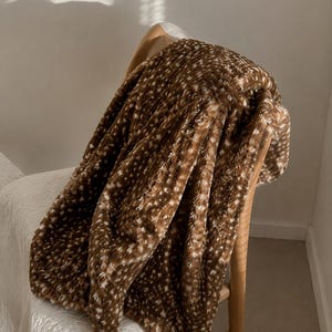 May include: A plush, textured throw blanket in a deep brown colour featuring a repeating pattern of small, white, star-like or speckled shapes. The fabric has a soft, fuzzy appearance with a dense pile, draped over a wooden chair frame.