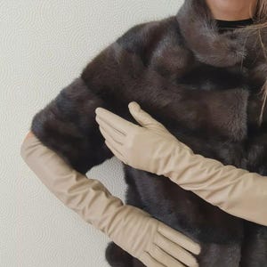 May include: A pair of long, beige leather gloves. The gloves are being worn by a person wearing a brown fur coat.