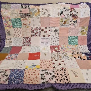 Könnte beinhalten: Ein Patchwork-Quilt mit verschiedenen Stoffen in Rosa, Weiß und gemusterten Designs. Einige Quadrate zeigen Disney-Figuren, Blumendrucke und Text. Der Quilt enthält ein Etikett mit dem Namen "Harper Bleu" und Geburtsdetails. Der Rand ist einfarbig lila.