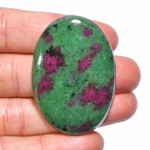 Könnte beinhalten: Ovaler Edelstein mit leuchtend grüner Basis und auffälligen magentafarbenen Einschlüssen. Die polierte Oberfläche reflektiert das Licht und hebt die natürlichen Muster und Texturen des Steins hervor. Ein einzigartiges Stück.