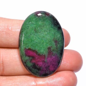 Könnte beinhalten: Oval geformter Edelstein mit einer auffälligen Farbmischung. Der Stein zeigt eine satte grüne Basis mit auffälligen Flecken in tiefem Magenta und schwarzen Akzenten. Die polierte Oberfläche hebt die natürlichen Muster und Texturen hervor.