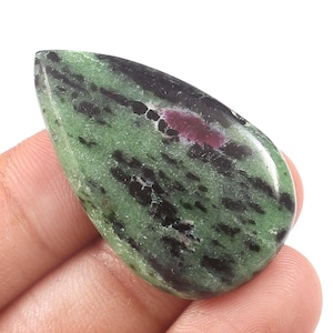 Könnte beinhalten: Ein polierter, tropfenförmiger Edelstein mit grünen, schwarzen und roten Farbtönen. Der Stein hat eine glatte Oberfläche mit dunklen grünen und schwarzen Adern und einem zentralen roten Einschluss. Der Edelstein wird in einer Hand gehalten.