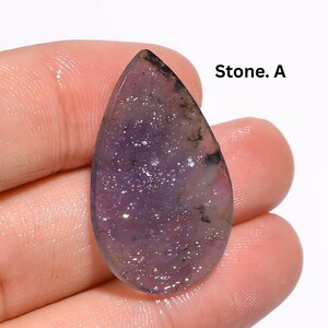 Peut inclure: Une pierre précieuse violette translucide en forme de poire avec une surface texturée et scintillante et des inclusions sombres. La pierre est marquée du texte Stone. A dans le coin supérieur droit. La surface reflète la lumière avec éclat.
