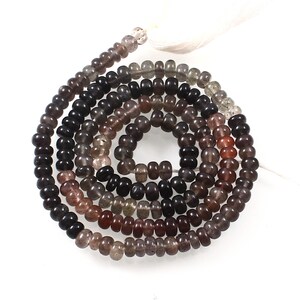 May include: A necklace of gemstone beads in shades of brown, black, and clear. The small, rounded beads are strung together, with a white tassel at the end. The beads are likely used for jewellery making.