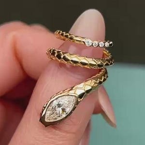 Könnte beinhalten: Goldfarbener Schlangenring mit einem Diamanten im Marquiseschliff am Kopf und kleinen Diamanten am Schwanz. Der Ring wickelt sich spiralförmig um den Finger und zeigt ein strukturiertes Schuppenmuster.