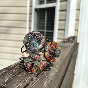 May include: Three crystal bracelets with copper wire wrapped around them. The bracelets are made of clear resin with various crystals and copper flakes embedded inside. The bracelets are stacked on top of each other on a wooden surface.