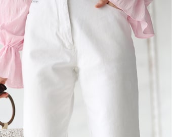May include: White high-waisted pants with a gray belt. The pants are paired with a pink ruffled top with long sleeves. A white and beige handbag is visible on the left side of the image.