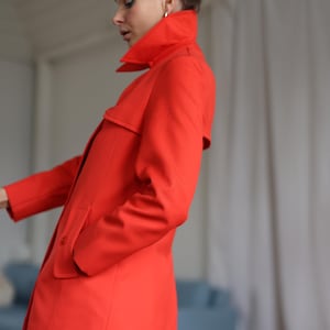 May include: A vibrant red coat with a high collar and a tailored fit. The coat features a classic design with a button closure and pockets. The bright color makes it a statement piece. The coat is a stylish outerwear option.