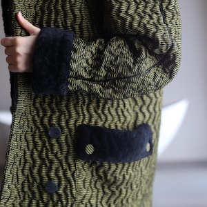 Puede incluir: Una chaqueta acolchada verde con ribetes negros y un bolsillo negro. La chaqueta tiene un patrón texturizado ondulado.
