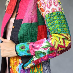 May include: A vibrant patchwork jacket in a mix of colours and patterns, including pink, green, red, and blue. The jacket has a quilted texture and black trim. The long sleeves display floral and geometric designs.