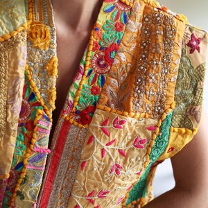 May include: A patchwork vest with intricate embroidery in shades of yellow, orange, green, and pink. The vest features a variety of floral and geometric patterns, with beaded and sequined accents. The design is a mix of textures and colors.