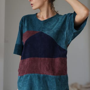 Puede incluir: Una camiseta de bloques de color verde azulado, burdeos y azul marino con cuello en V. La camiseta de manga corta tiene un ajuste relajado y una apariencia texturizada. El diseño de bloques de color presenta rayas horizontales y en ángulo.