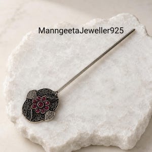 Peut inclure: Une épingle à cheveux en argent avec une tête florale en métal oxydé ornée de sept petites pierres rondes rose foncé disposées en fleur. Le texte ManngeetaJeweller925 est visible dans la partie supérieure de l'image.
