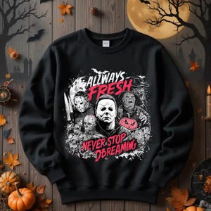 May include: Black sweatshirt with a Halloween-themed graphic. The design features the text "ALWAYS FRESH NEVER STOP DREAMING" with images of horror movie characters, including Michael Myers, Jason Voorhees, and Freddy Krueger. A pumpkin is also included in the design.