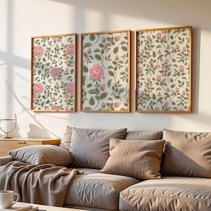 May include: Three framed floral art prints featuring pink roses and green leaves on a cream background. The prints are displayed above a gray sofa with pillows and a wooden cabinet. A coffee table and decorative items complete the room.