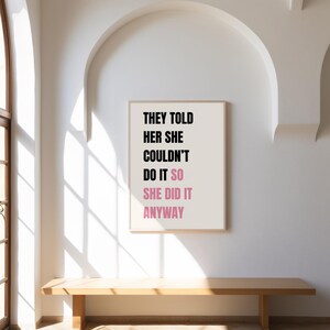 May include: A framed print with the text "THEY TOLD HER SHE COULDN'T DO IT SO SHE DID IT ANYWAY" in black and pink. The print hangs on a white wall above a wooden bench. The room has an arched doorway.