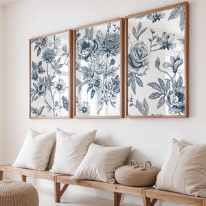 Pu&ograve; includere: Tre opere d'arte incorniciate con un design floreale blu. L'opera d'arte &egrave; esposta sopra una panca di legno con cuscini bianchi e un cestino intrecciato. Il motivo floreale presenta dettagliate illustrazioni botaniche in tonalit&agrave; di blu su sfondo bianco.