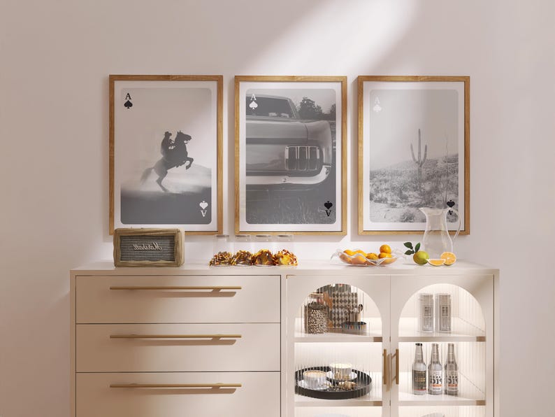 Op de afbeelding: Drie ingelijste zwart-wit prints met houten frames. De prints tonen een cowboy op een paard, een auto en een woestijnlandschap. De Aas van Schoppen staat boven en onder elke print. Een houten bord leest "Welcome".