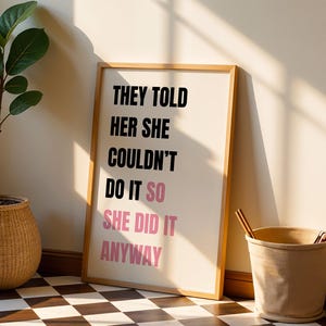 May include: A framed print with the text "THEY TOLD HER SHE COULDN'T DO IT SO SHE DID IT ANYWAY" in black and pink. A potted plant in a woven basket and a beige bucket are next to the framed print. The floor is a black and white checkered pattern.