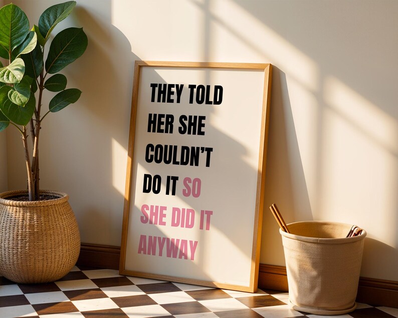 May include: A framed print with the text "THEY TOLD HER SHE COULDN'T DO IT SO SHE DID IT ANYWAY" in black and pink. A potted plant in a woven basket and a beige bucket are next to the framed print. The floor is a black and white checkered pattern.