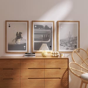 Op de afbeelding: Drie ingelijste kunstprints met een speelkaartthema. De prints tonen een paard en ruiter, een klassieke auto en een woestijnlandschap. De frames zijn lichtbruin en de kunst is in zwart-wit.