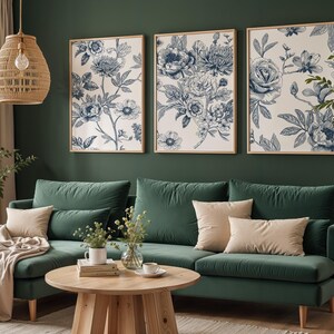 Pu&ograve; includere: Tre stampe floreali incorniciate con illustrazioni botaniche blu e bianche sono appese sopra un divano in velluto verde con cuscini beige. Un tavolino rotondo in legno e una lampada a sospensione in vimini completano l'arredamento.