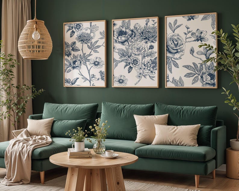Pu&ograve; includere: Tre stampe floreali incorniciate con illustrazioni botaniche blu e bianche sono appese sopra un divano in velluto verde con cuscini beige. Un tavolino rotondo in legno e una lampada a sospensione in vimini completano l'arredamento.