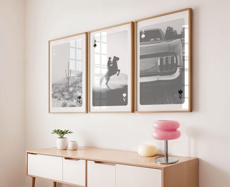 Op de afbeelding: Drie ingelijste zwart-wit prints met speelkaartmotieven. De prints tonen een woestijnlandschap, een cowboy op een steigerend paard en een klassieke auto. De lijsten zijn licht van kleur, boven een houten kast.