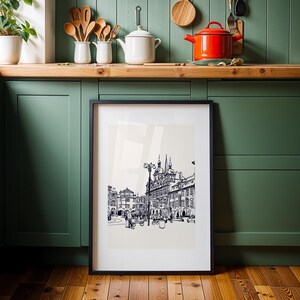 May include: A framed black and white architectural print featuring a detailed street scene with buildings, streetlights, and figures. The artwork is displayed against a neutral background, with a black frame. The print is set against a backdrop of a green kitchen.