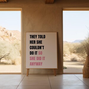 May include: A framed print with the text "THEY TOLD HER SHE COULDN'T DO IT SO SHE DID IT ANYWAY" in black and pink. The print is on a wooden easel in front of a window with a desert landscape.