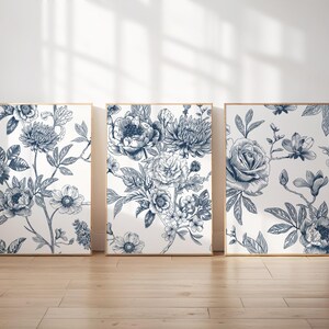 Pu&ograve; includere: Tre stampe artistiche floreali incorniciate. Ogni stampa presenta una diversa disposizione di fiori blu e bianchi, tra cui rose, peonie e altri fiori. L'opera d'arte &egrave; esposta su un pavimento in legno chiaro.