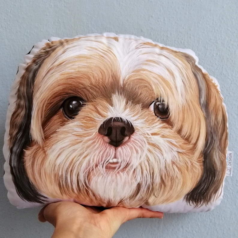 May include: A plush pillow featuring a close-up illustration of a Shih Tzu dog's face. The dog has brown and white fur, with a pink nose and brown eyes. The pillow is white with a black border.