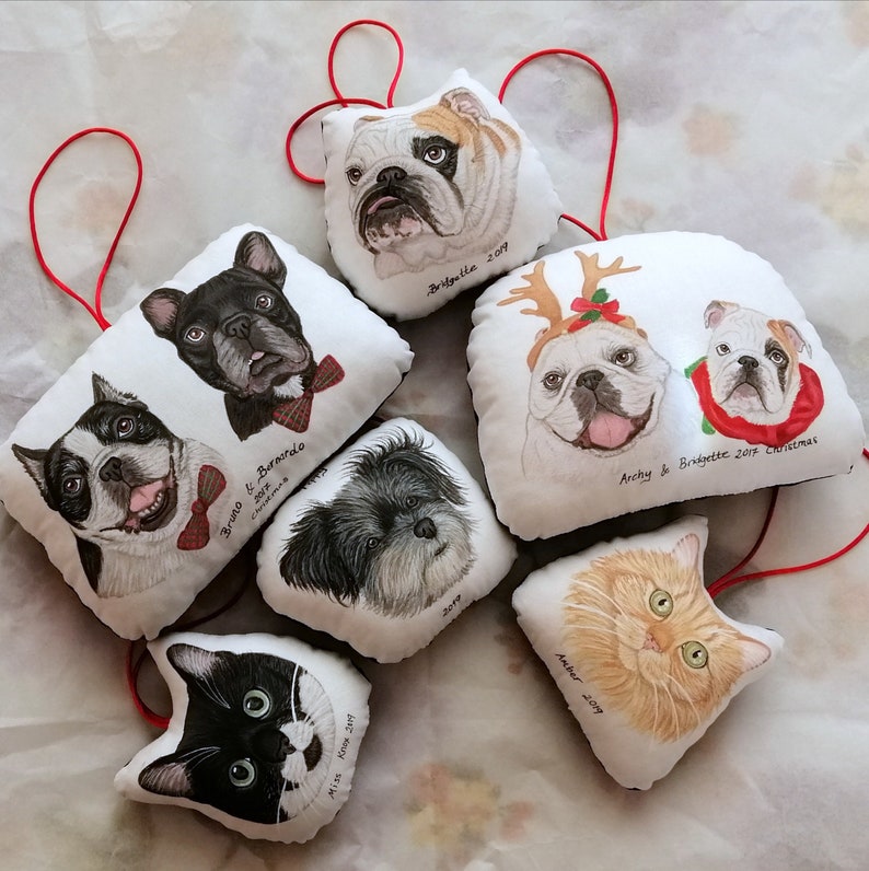 Puede incluir: Un conjunto de siete adornos de tela blanca con retratos pintados a mano de perros y gatos. Cada adorno presenta un animal diferente con un nombre personalizado y un a&ntilde;o. Los adornos est&aacute;n decorados con detalles rojos y verdes, lo que los hace perfectos para la temporada navide&ntilde;a.