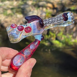 May include: A red and white glass pipe with a swirl design and a black and white patterned section. The pipe has three red glass spheres with glitter inside.