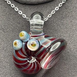 May include: A glass pendant necklace with a silver chain. The pendant features a swirling design of red, white, and blue glass, with three small blue orbs. The pendant is approximately 2 inches long.