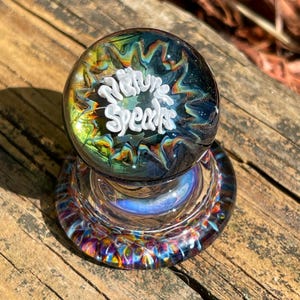 May include: A glass paperweight with a swirling blue, green, and yellow pattern. The top of the paperweight has a white inscription that reads "Nature Speaks".