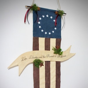 A decorative vertical banner made from muslin fabric for your primitive patriotic decor.   Featuring painted navy blue field with stars featuring the 13 original colonies.   On the  lower half you will find  hand painted stripes in deep burgundy with a stained muslin banner running horizontally across the banner with the words " life liberty and the pursuit of happiness"    Perfect for your Patriotic holidays