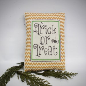 May include: A yellow and white chevron patterned pillow with the text "Trick or Treat" in black lettering and two black spider silhouettes.