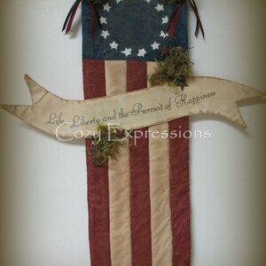May include: A rustic American flag banner with 13 red and white stripes and a blue canton with 13 white stars. The banner has a white ribbon with the text "Life, Liberty and the Pursuit of Happiness" and is decorated with moss.