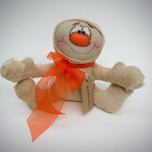 Primitive halloween seated fabric mummy decoration with an orange bow and Karloff tag around his neck