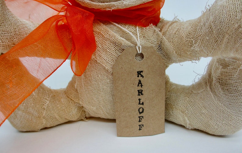 May include: A handmade burlap mummy doll with an orange ribbon and a brown tag that says "KARLOFF".