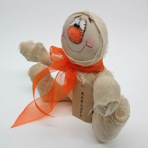 May include: A handmade white fabric mummy doll with orange fabric accents and a tag that reads "KARLOFFE".