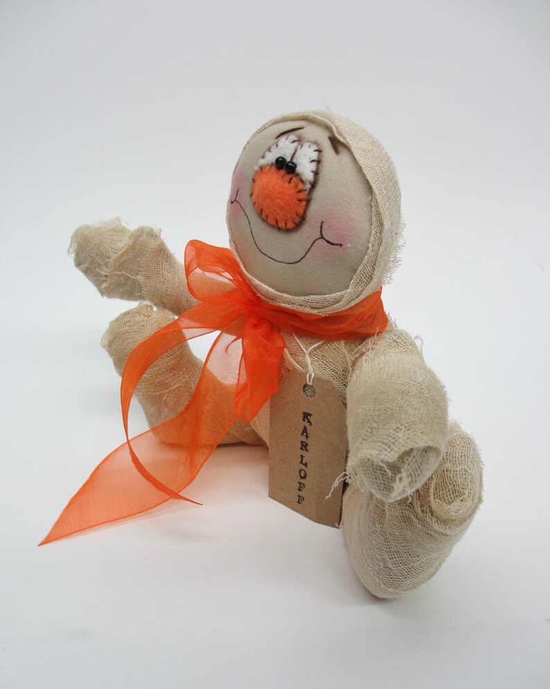 May include: A handmade white fabric mummy doll with orange fabric accents and a tag that reads "KARLOFFE".