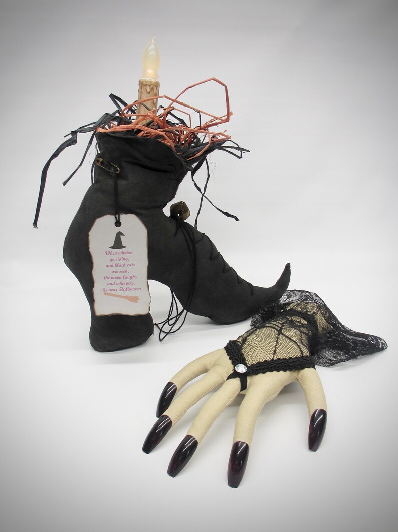 May include: A black witch's boot with a lit candle on top, surrounded by straw. A black lace glove with long, dark nails is on the right side of the image. The boot has a tag that reads: "When witches go riding, and black cats are seen, the moon laughs and whispers, 'Tis near Halloween.'"