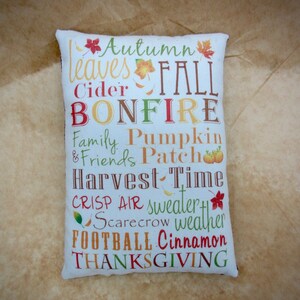 May include: White pillow with a colorful autumn-themed design. The text on the pillow reads "Autumn Leaves Fall Cider Bonfire Family Pumpkin & Friends Patch Harvest Time Crisp Air Sweater Scarecrow Weather Football Cinnamon Thanksgiving".