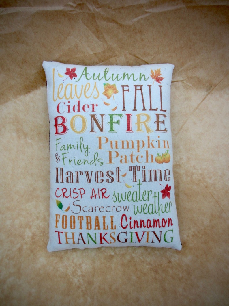 May include: White pillow with a colorful autumn-themed design. The text on the pillow reads "Autumn Leaves Fall Cider Bonfire Family Pumpkin & Friends Patch Harvest Time Crisp Air Sweater Scarecrow Weather Football Cinnamon Thanksgiving".