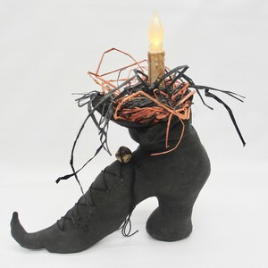 May include: A black witch's boot with a pointed toe and a high heel. The boot is decorated with a black and orange nest and a lit candle.