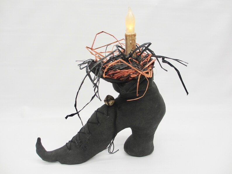 May include: A black witch's boot with a pointed toe and a high heel. The boot is decorated with a black and orange nest and a lit candle.
